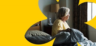 A woman stares out the window as she sits on the side of her bed