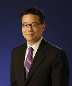 Dr. John G. Lee smiling in business attire.