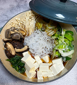 Sukiyaki with assorted mushrooms displayed in teal blue wok on gray countertop.