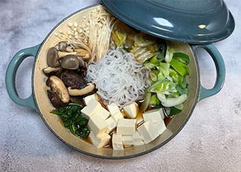 Sukiyaki with assorted vegetables sits in teal blue wok on gray counter.