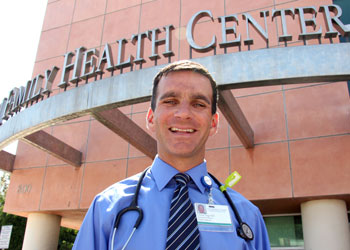 uci health family medicine dr. charles vega stands in front of the uci health family medicine center santa ana wearing a blue shirt and stethoscope and name badge, smiling