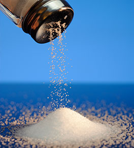 Salt sprinkling out of shaker into a pile on a blue background.