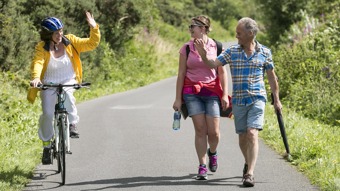 Cyclist passing two walkers on cycle path, both parties waving to each other