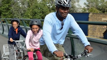 A man and two young girls riding a tandem bike over a bridge