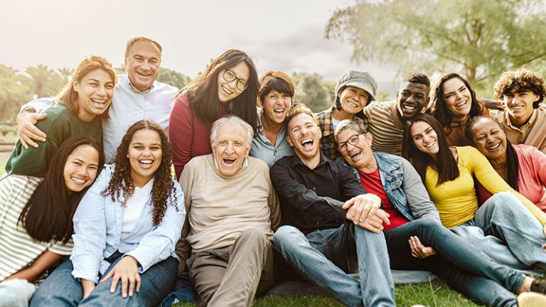 A group of people of different races and ages smiling together in a park. 