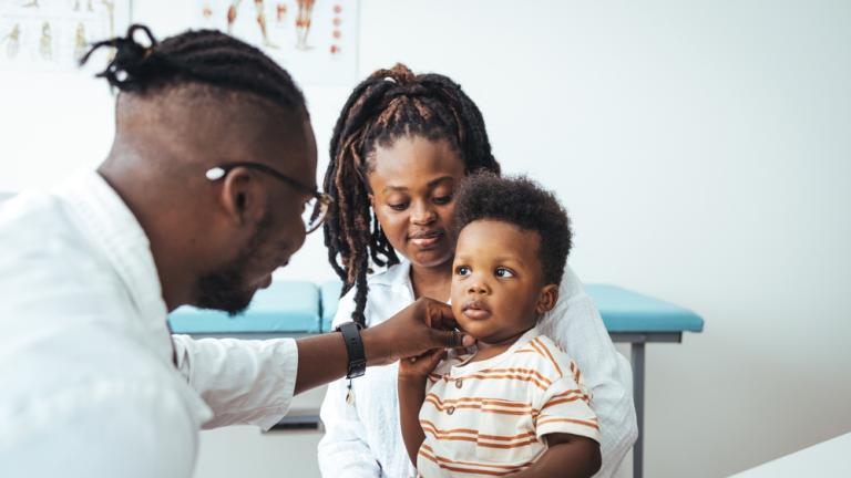 Image of a child sitting on his mother's lap being checked out by a doctor