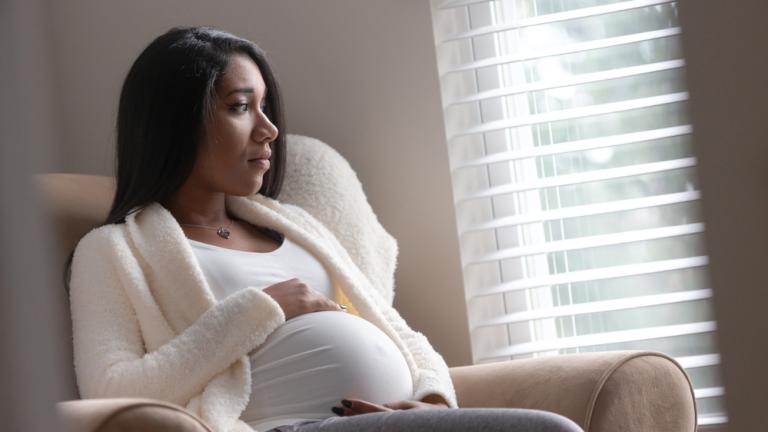 A pregnant woman in deep thought looks out a window