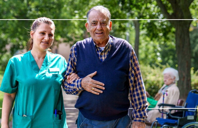 older man and nurse walking in wooded area with an older women in a wheelchair in the background