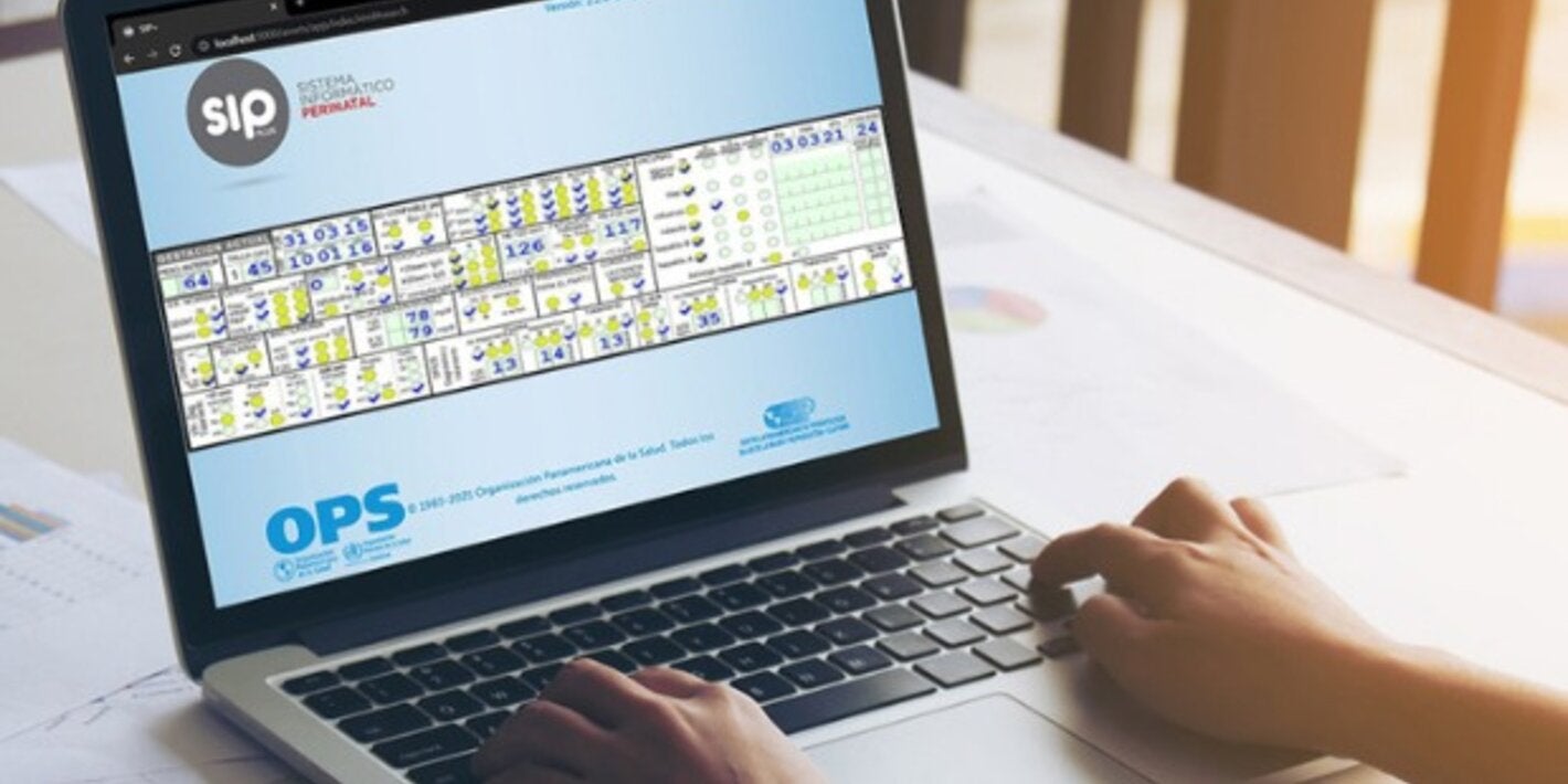 Computadora sobre un escritorio. En la pantalla se ve el Sistema de Información Perinatal. Hay unas manos sobre el teclado.