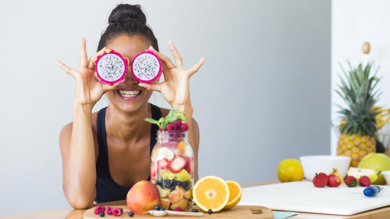 woman smiling while holding slices of dragonfruit in front of her eyes