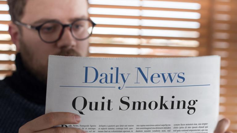 Man reading Quit Smoking headlined newspaper