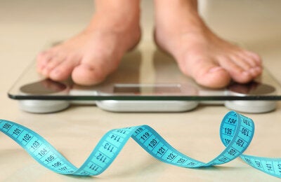 Photo of a blue measuring tape in the front and an electronic weight bascule with a pair of feet over it