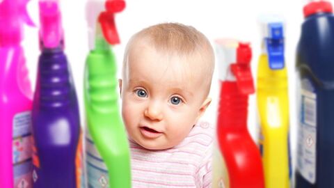 Ein Baby schaut zwischen bunten Putzmittelflaschen in die Kamera