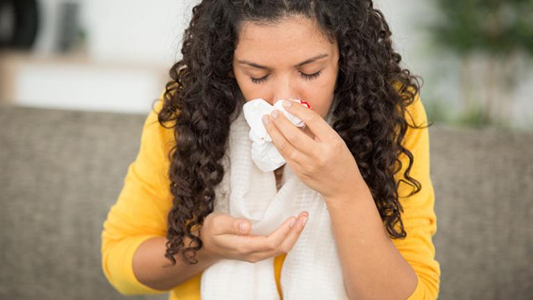 Women in a yellow shirt holding a tissue up to her nose for a nosebleed