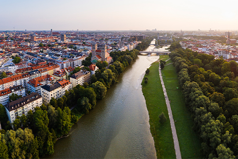 Flyfoto av München med en elv, trær og en gangvei langs elven.