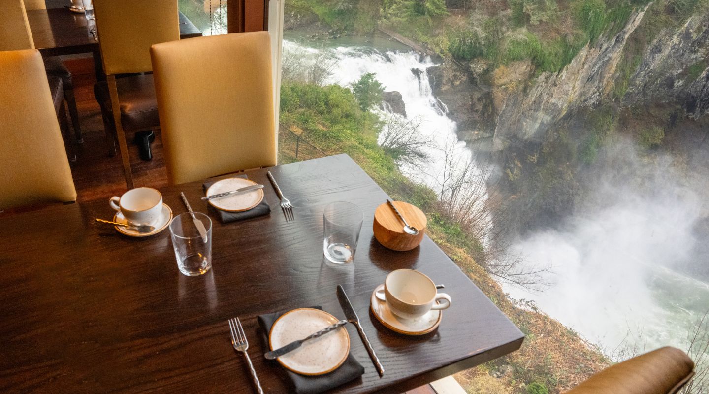 A Table With Plates And Cups On It By A Body Of Water