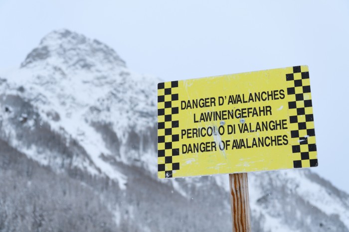 Close-up of a yellow avalanche warning board in front of a snowy mountain