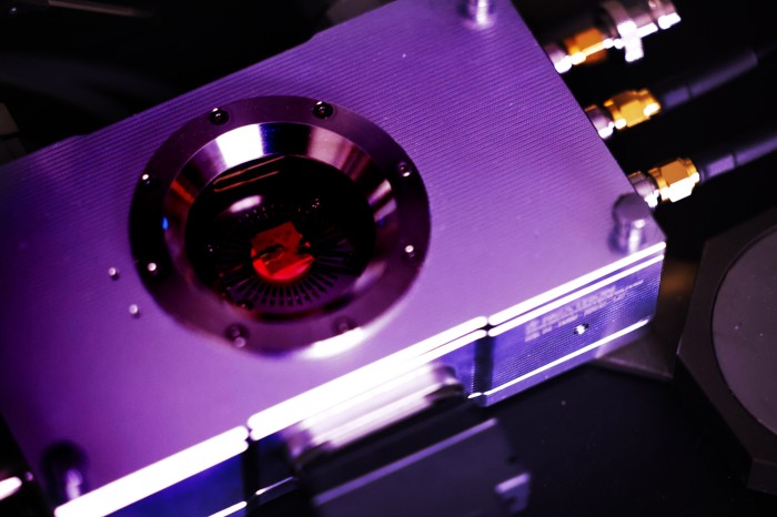 Close up photograph of a small, square, solid-state memory device visible through a circular window in a rectangular box glowing red as it is subjected to very high temperatures