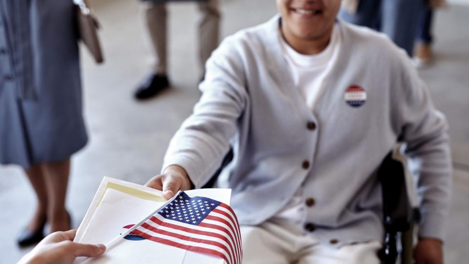 A person in a wheelchair receives voting materials.