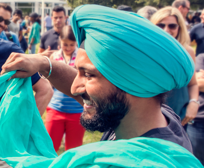 Photo d’un homme avec un turban qui sourit en nouant le turban de quelqu’un d’autre.