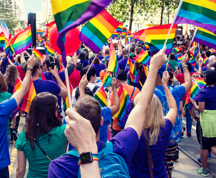 Photo d’une foule qui défile en brandissant des drapeaux arc-en-ciel. 