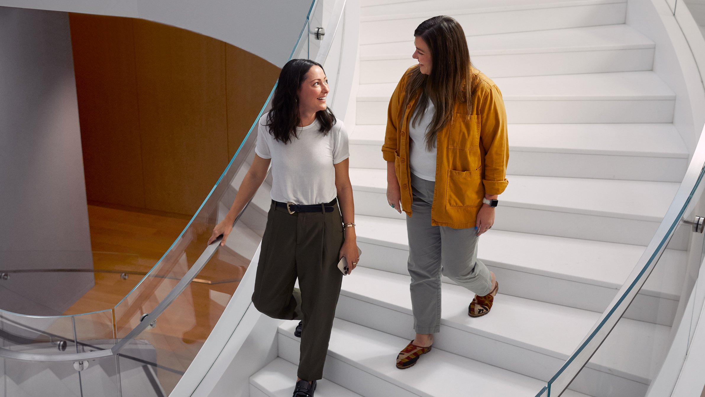 Two Apple colleagues walking down a broad, curving staircase. 