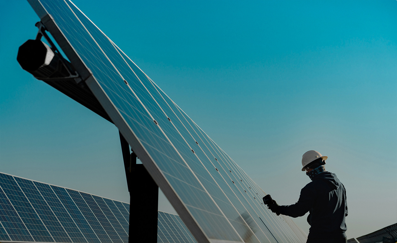 Un homme portant un casque de chantier travaille sur un grand panneau solaire en extérieur.