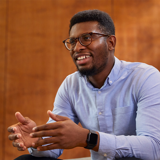 Chidi, seated and smiling, looking off to the side.