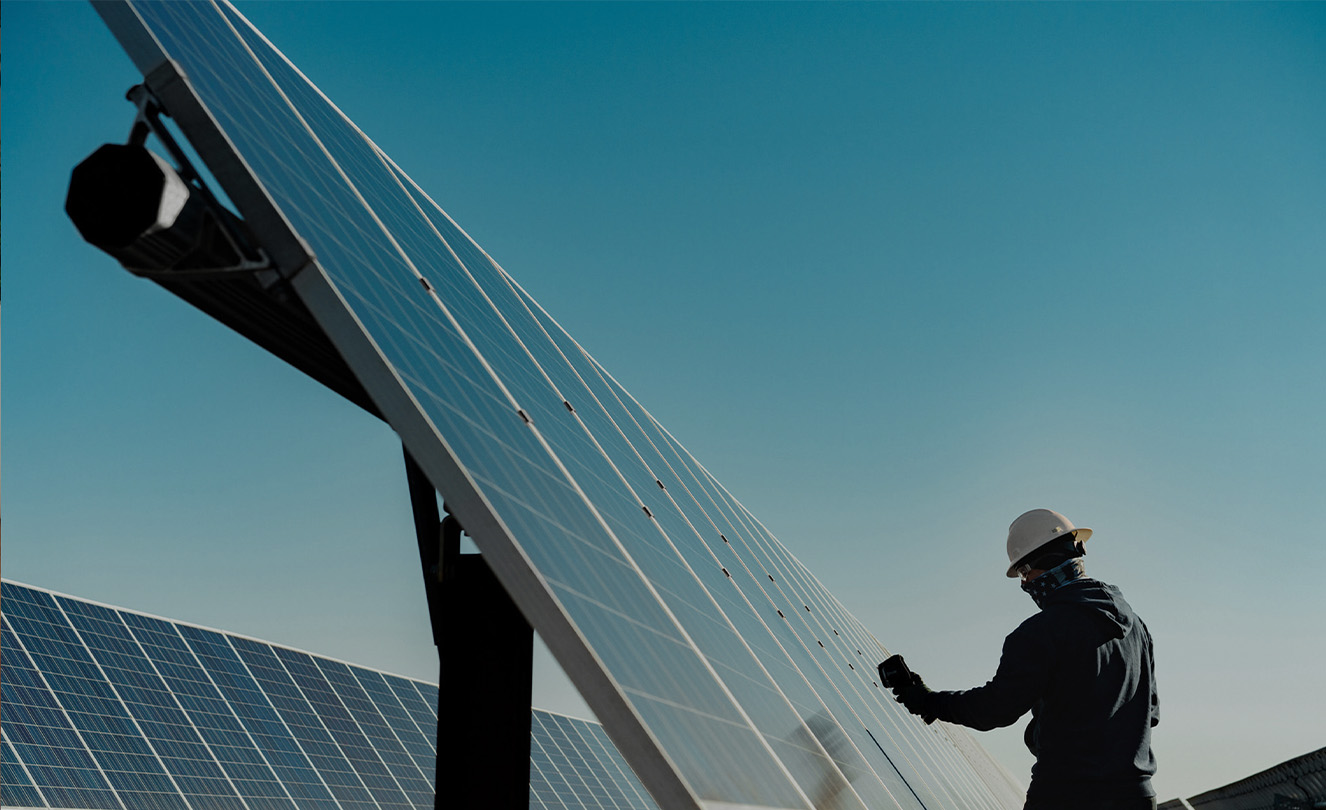 A person in a hard hat working on a large solar panel outside.