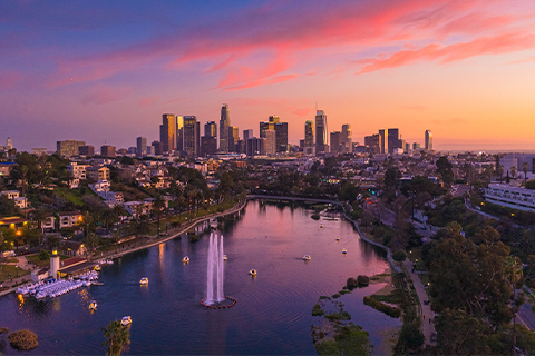 Aerial view looking toward Los Angeles skyscrapers with a park and a lake in the foreground.