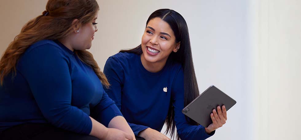 A Carissa segura um iPad e conversa com outra funcionária da Apple Retail.