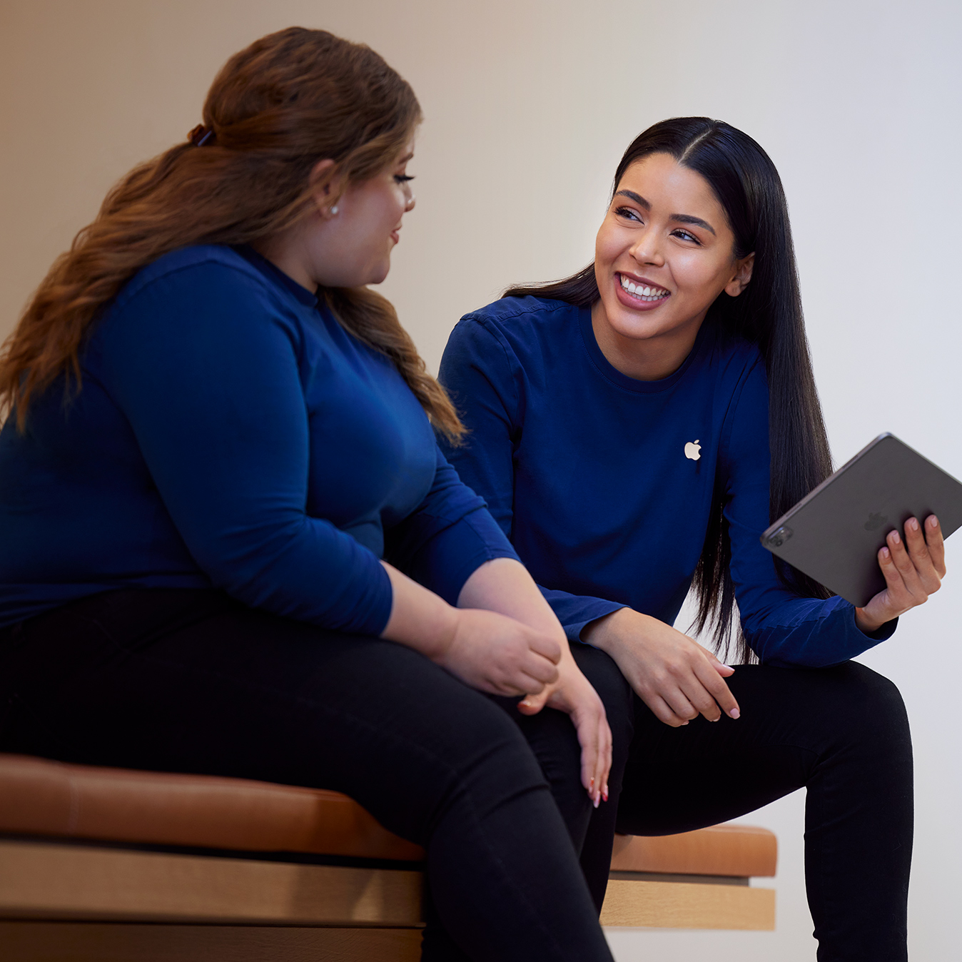 A Carissa segura um iPad e conversa com outra funcionária da Apple Retail.