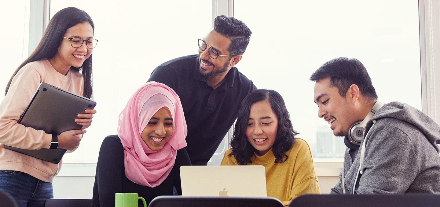 Apple employees gather for a discussion while looking at one employee’s MacBook.