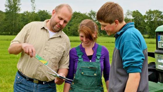 Landwirt mit zwei Auszubildenden stehen vor einem Feld