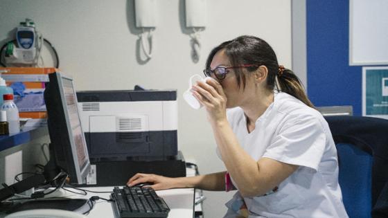 Ärztin im Krankenhaus sitzt am Schreibtisch und trinkt aus einer Tasse