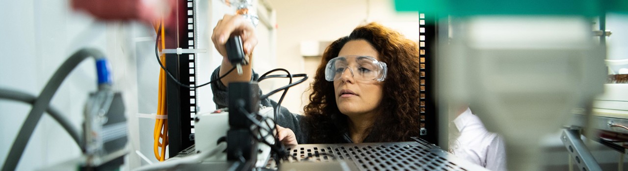 Woman in safety glasses plugging in a cord.