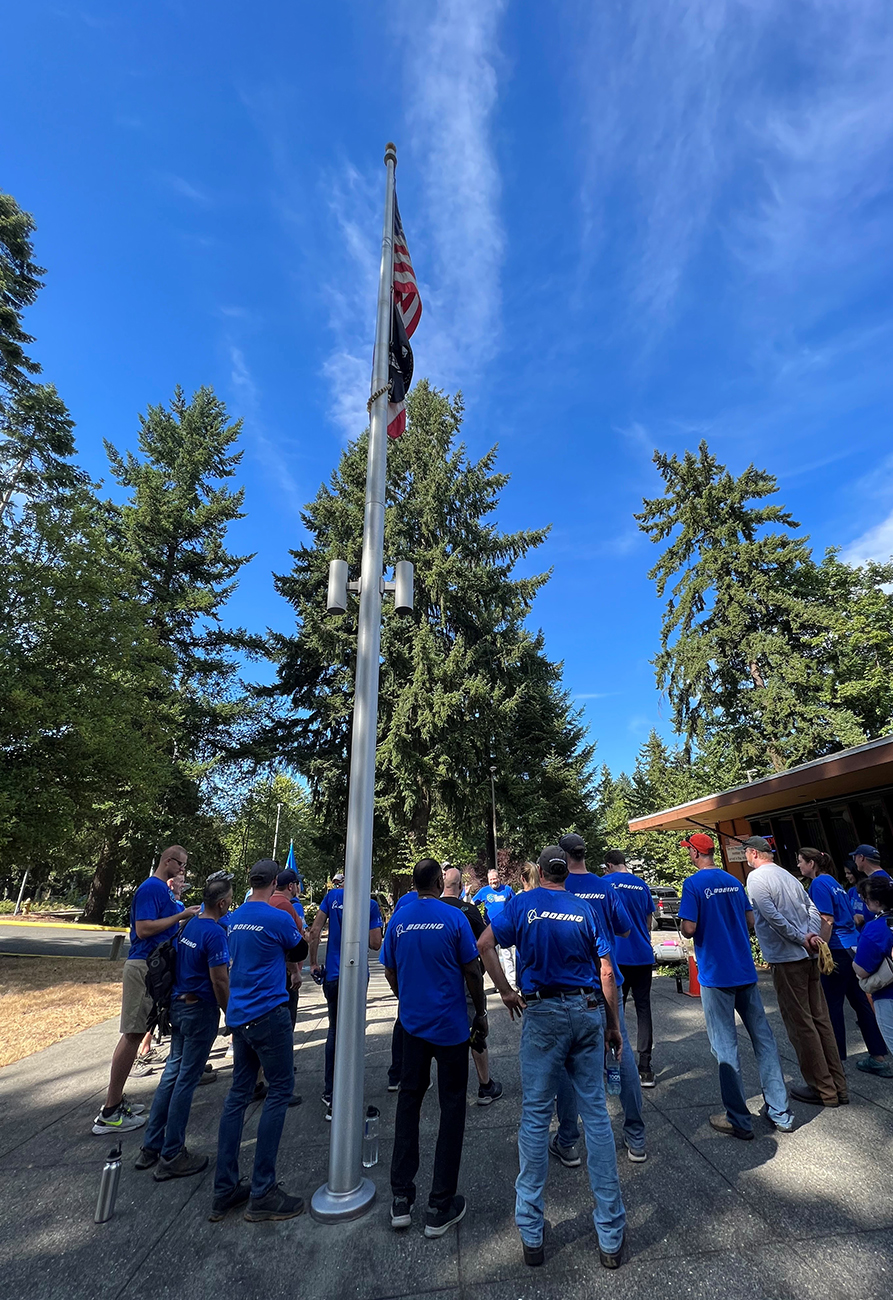 A bunch of people standing around a raised US flag