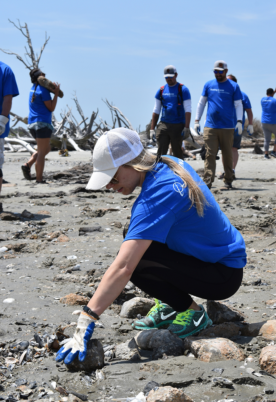 Boeing employee cleaning land with others helping in the background