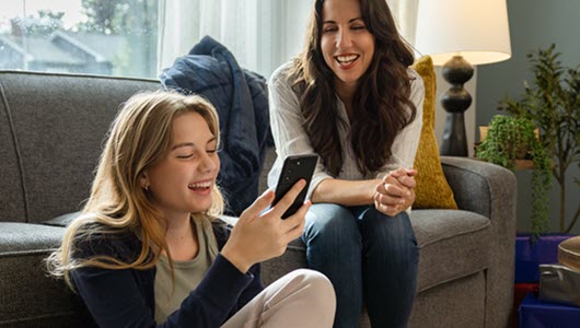 Daughter smiling at her new phone while her mom looks on.