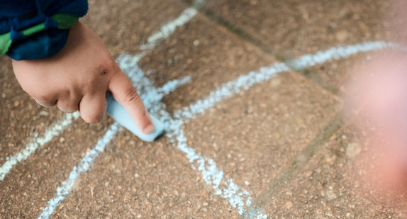 Eine Hand malt mit einem blauen Kreidestift Striche auf den Boden. 