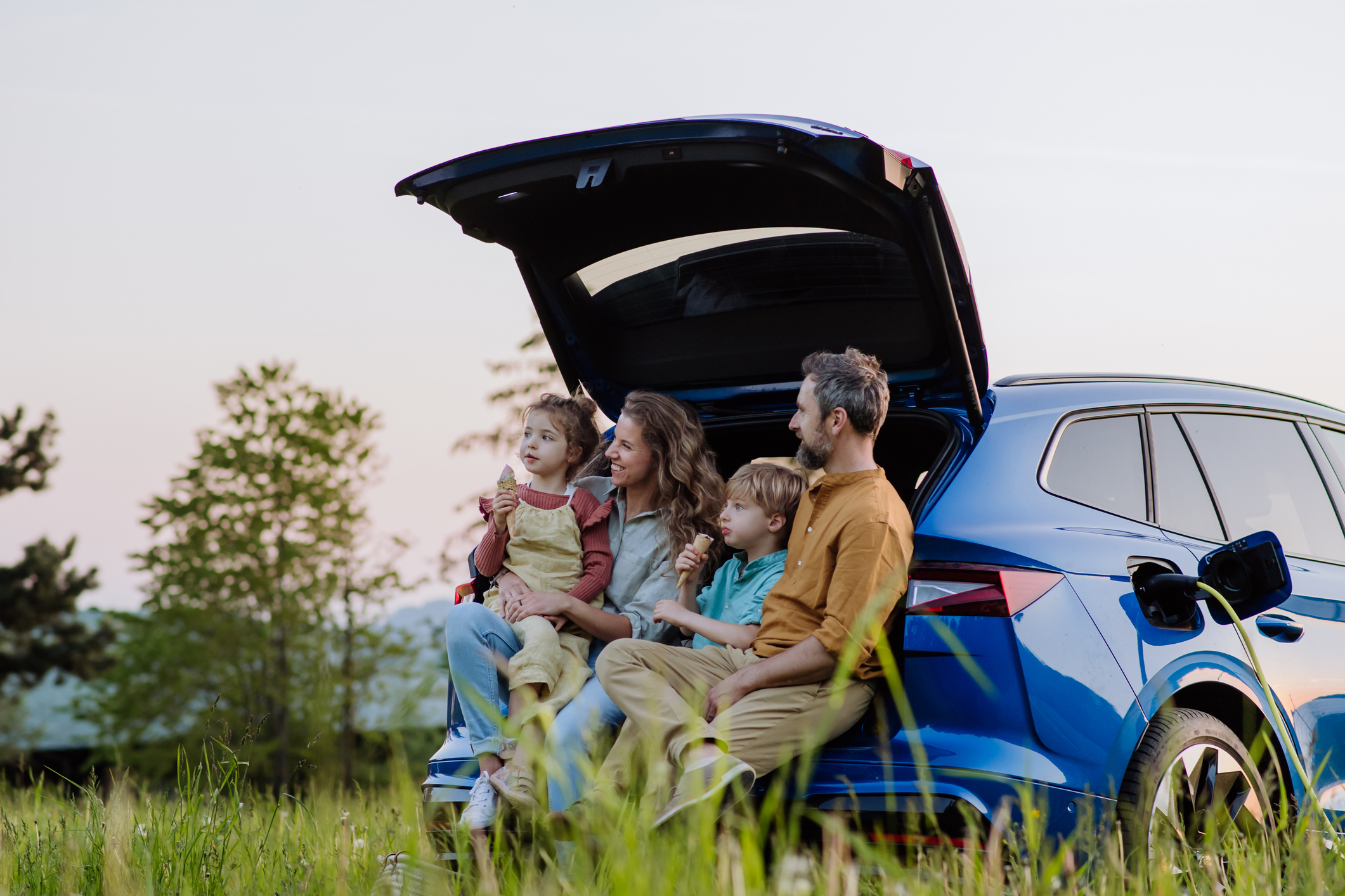 Family sitting at the boot of a car enjoying the countryside