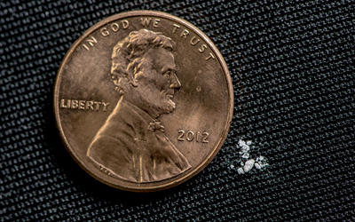 Black background. Photo of a penny. Next to the penny is a tiny amount of a white powder.