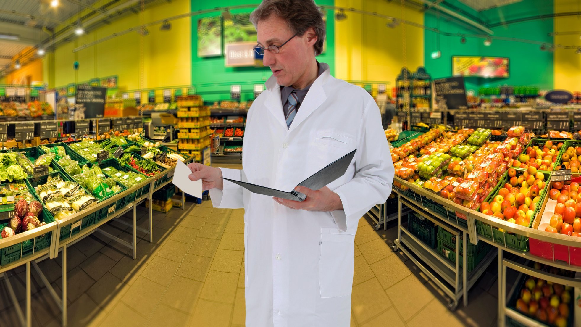 Mann im weißen Kittel und Mappe in der Hand steht im Supermarkt.