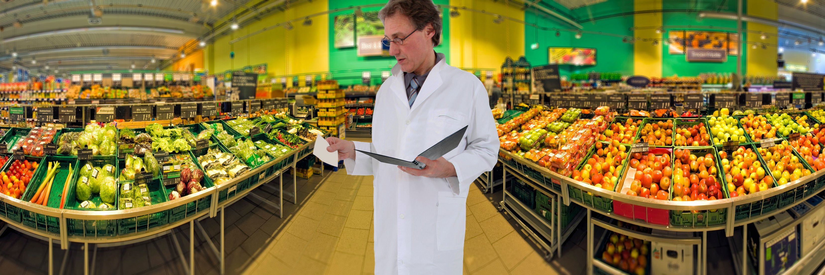 Mann im weißen Kittel und Mappe in der Hand steht im Supermarkt.