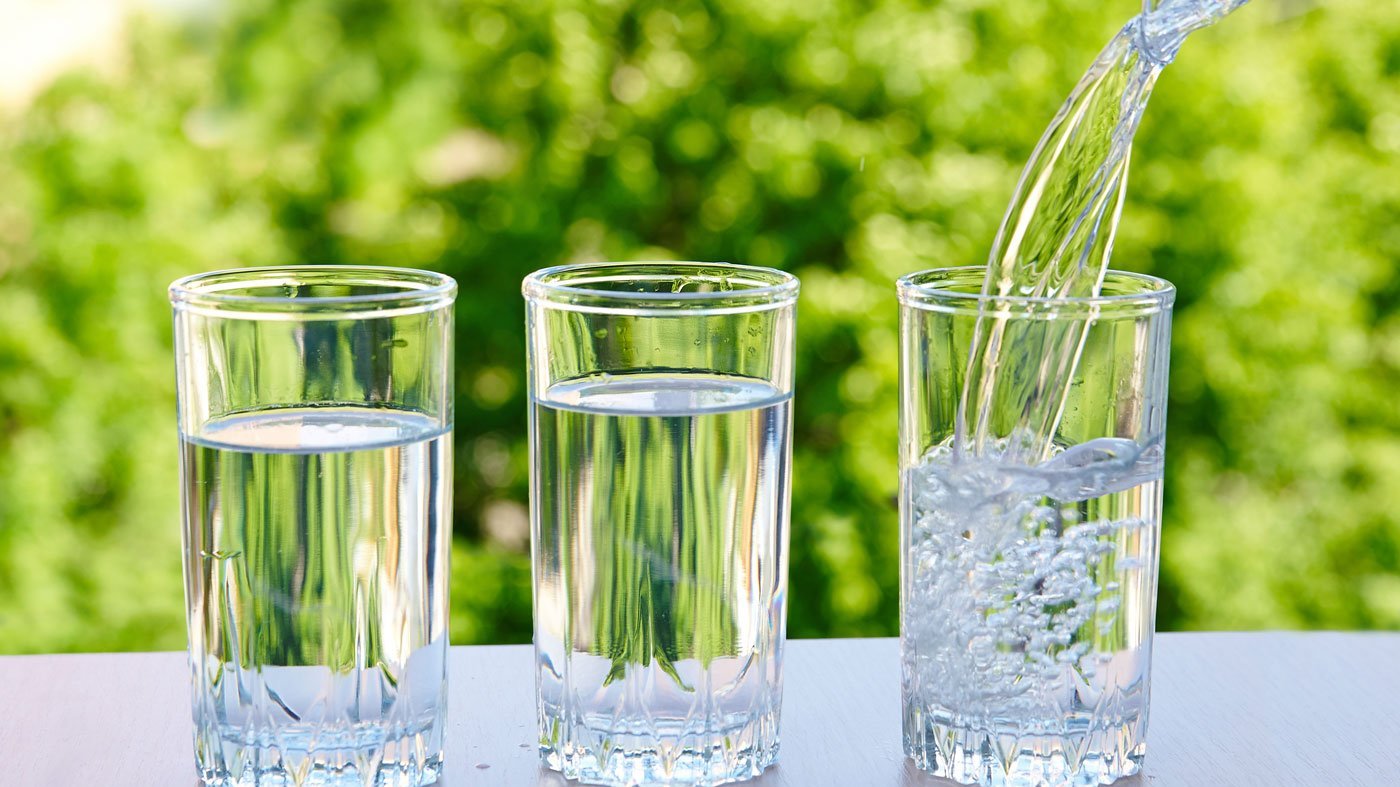 Drei volle Wassergläser stehen nebeneinander, eins wird befüllt