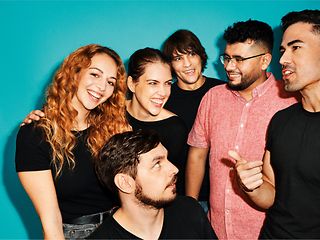 A group of young people stand close together, holding a lively discussion.