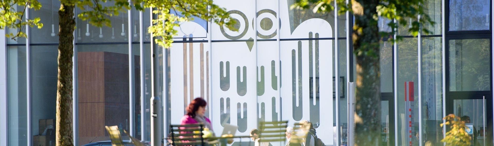 Ausschnitt eines Glasbaus mit großem weißen Logo der Universität des Saarlandes auf den Fenstern