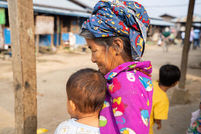 A woman in a camp for displaced people in Kachin State, Myanmar, holds a young child. It is estimated that more than 3 million people across the country have been forced to flee their homes as conflict surges between the Myanmar Armed Forces and various armed groups. March 2024. Photo: OCHA/Christina Powell.