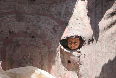 Jasser, a 7-year-old child from Gaza, peers through a tear in the fabric of a worn-out tent. 