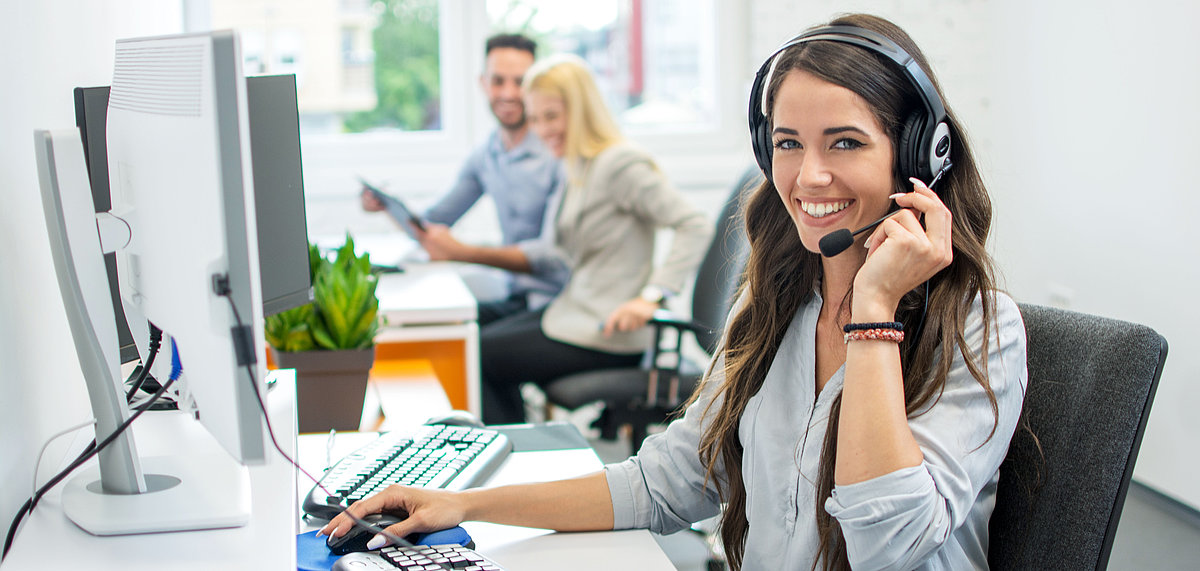 Frau mit Headset sitzt vor einem Computer